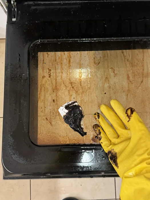 Gloved hand scraping burnt-on residue out of an oven during a Budapest deep clean